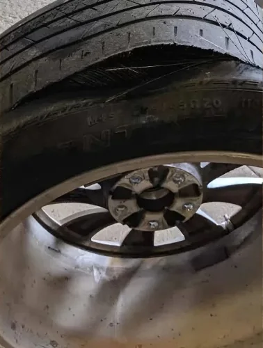 Close-up of a tire ruptured through the tread and sidewall, internal cords exposed on a bent rim